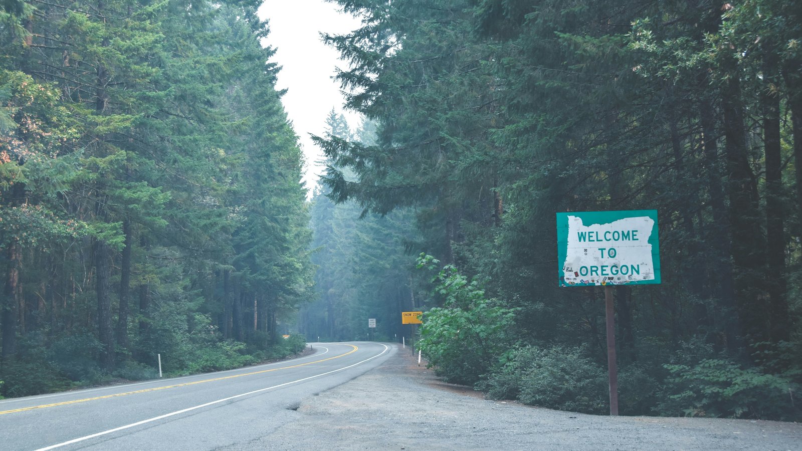 A sign reading “Welcome to Oregon” on a roadside in a forest