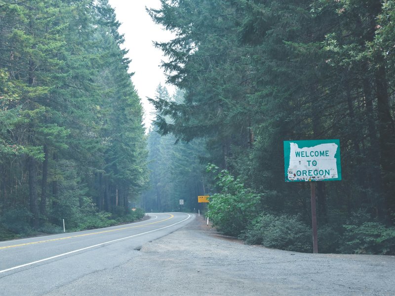 A sign reading “Welcome to Oregon” on a roadside in a forest