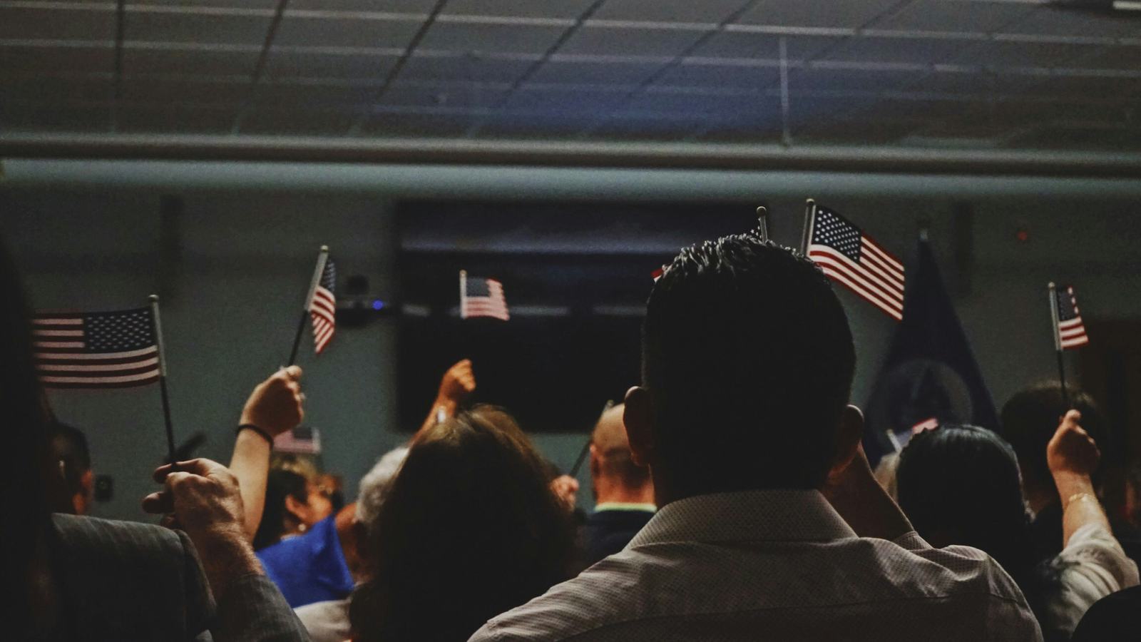 Group of people, likely new citizens at a citizenship ceremony, holding small American flags