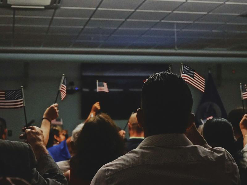 Group of people, likely new citizens at a citizenship ceremony, holding small American flags