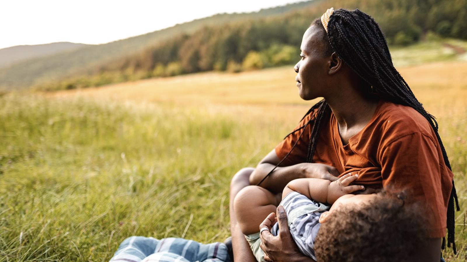 Woman breastfeeding an infant in a sunny meadow