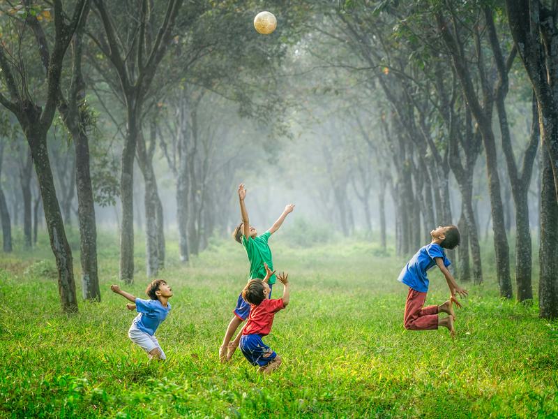 Kids playing with a ball outdoors, under trees